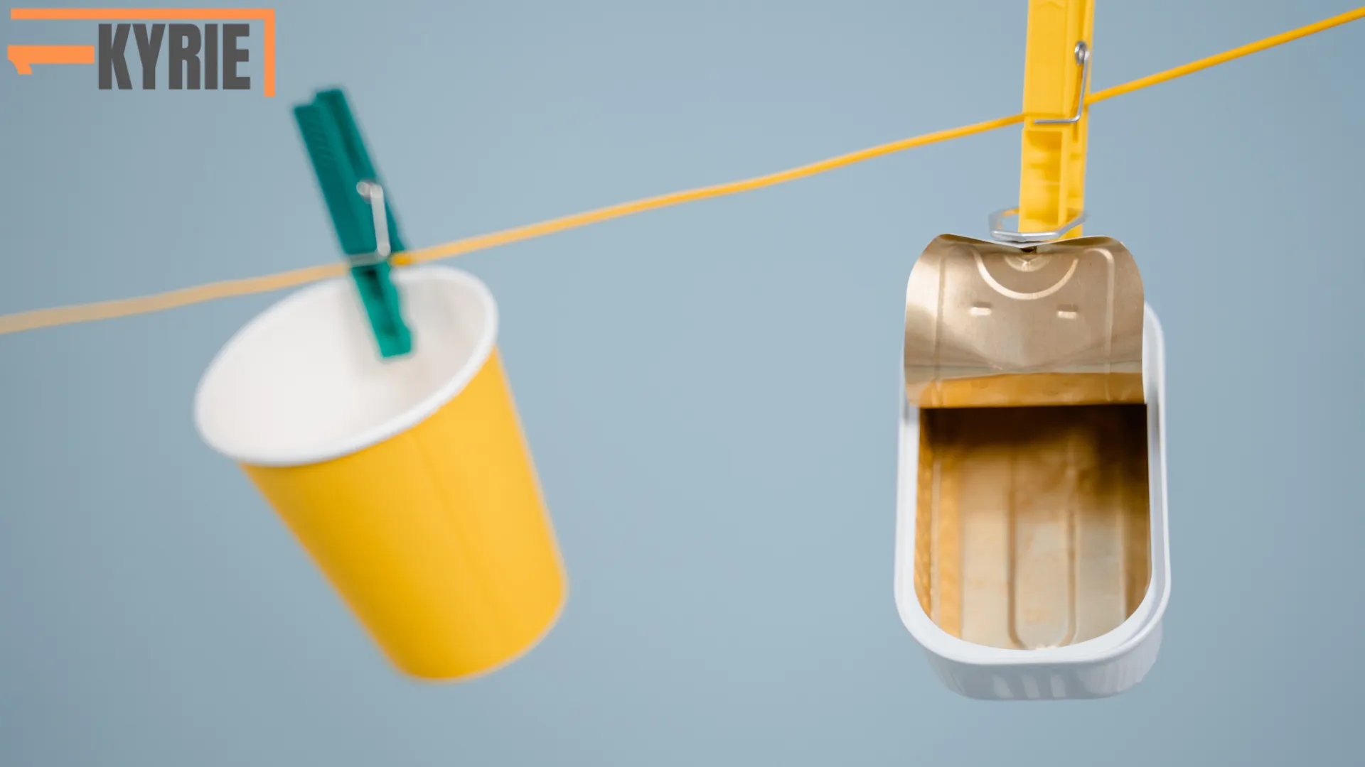 The image shows a yellow paper cup and a tin can hanging on a clothesline with clothespins, symbolizing waste materials. **Can you recycle Styrofoam?** Not easily, as it’s tricky to process compared to materials like paper and metal.