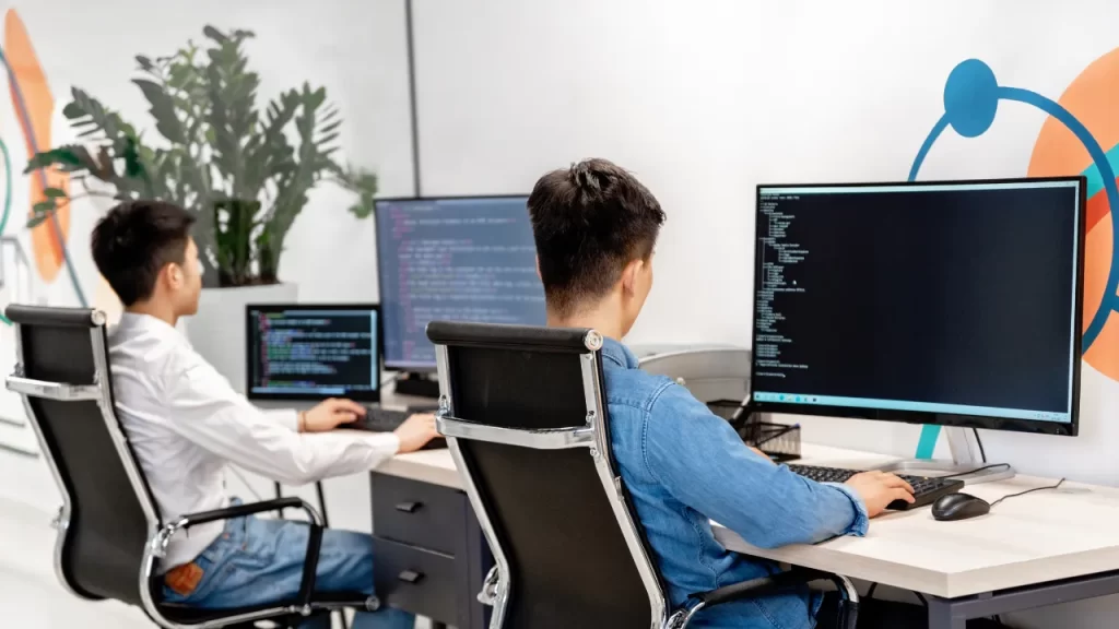 Developers collaborating on co-development software with dual monitors for coding and debugging