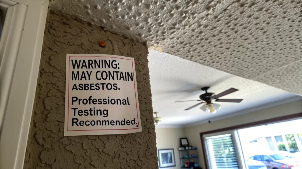 Popcorn ceiling with a warning label about possible asbestos exposure risks.